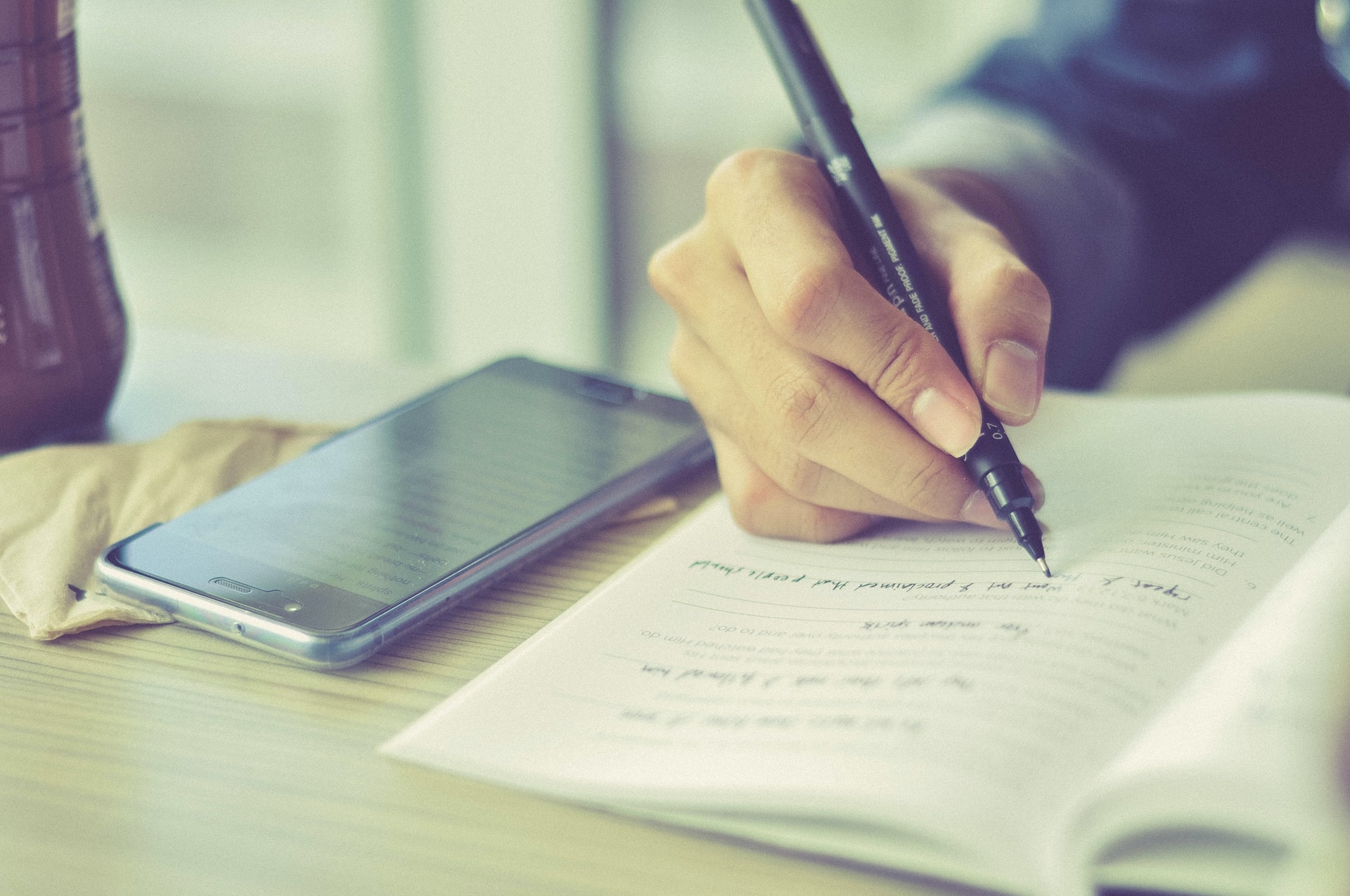 person writing on paper next to smartphone