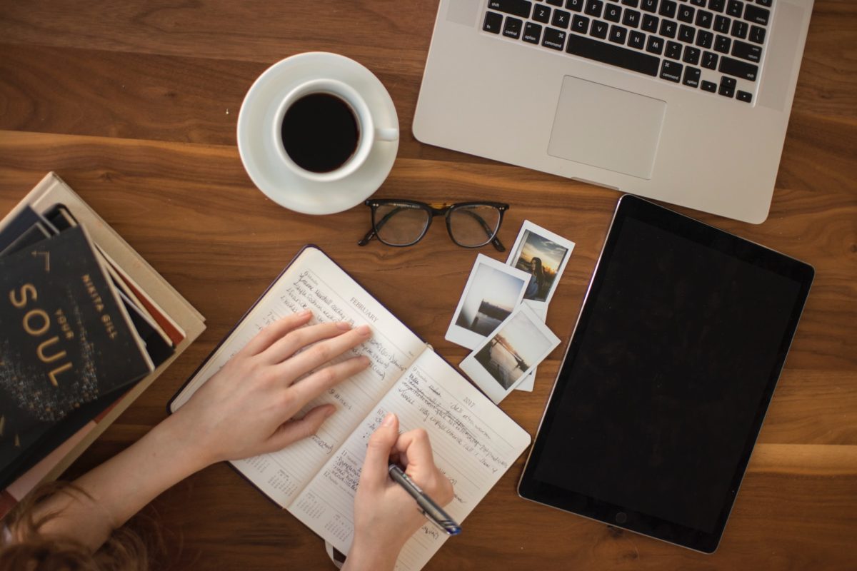 a person writing into notebook next to laptop 